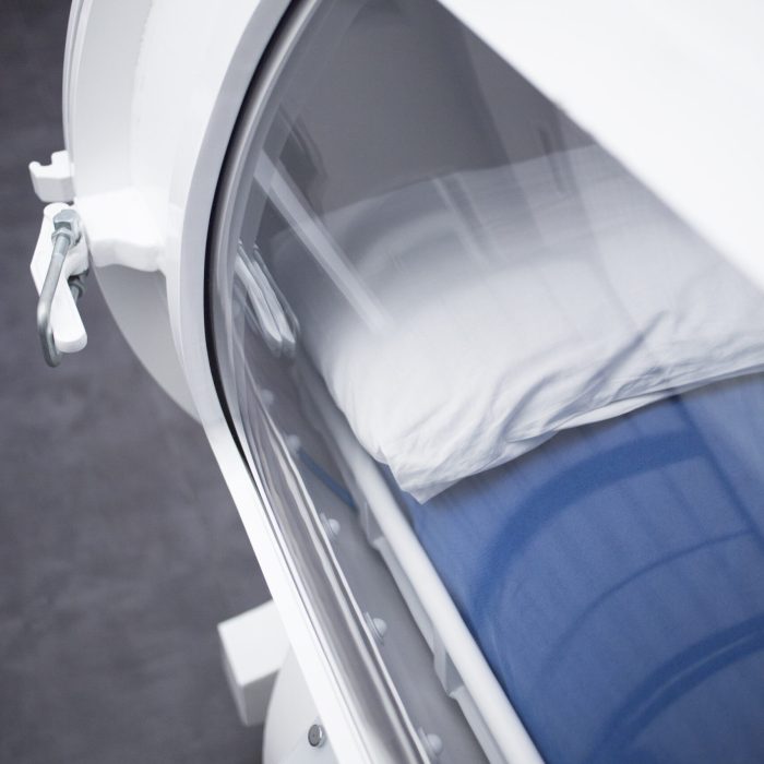 Hyperbaric Oxygen Therapy (HBOT) chamber tank used for specialised medical treatment for injuries in hospital clinic. Exterior viewing window and reflection with pillow and bed inside.