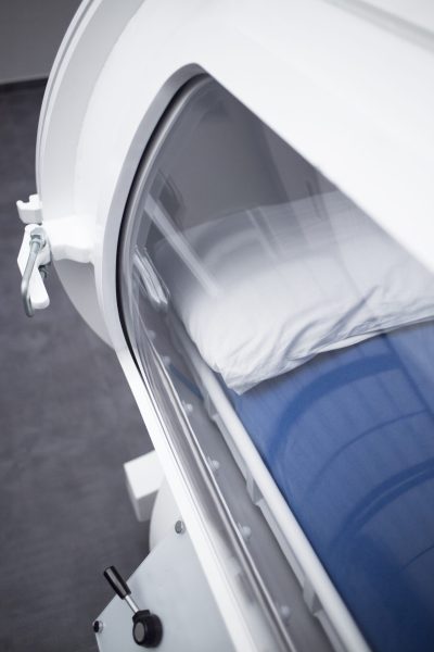 Hyperbaric Oxygen Therapy (HBOT) chamber tank used for specialised medical treatment for injuries in hospital clinic. Exterior viewing window and reflection with pillow and bed inside.